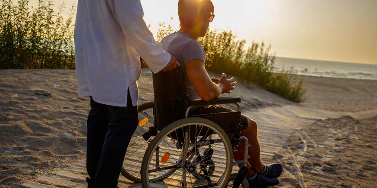 Support worker with personin wheelcahir on the beach
